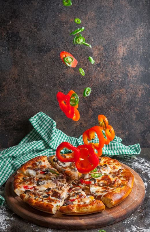 Pizza auf einem Holzbrett mit frischen Paprika – rustikal und dunkel in Szene gesetzt